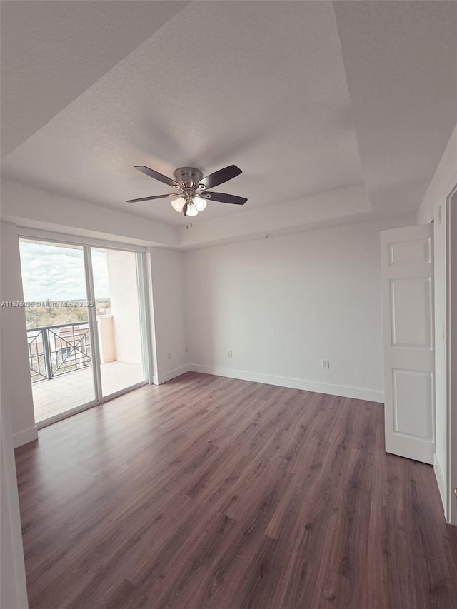 unfurnished room with a tray ceiling, baseboards, dark wood-style flooring, and ceiling fan