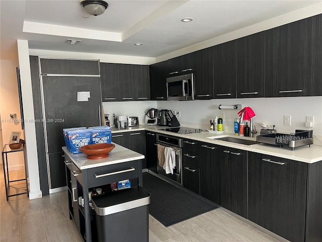 kitchen with sink, stainless steel appliances, a raised ceiling, and light hardwood / wood-style flooring