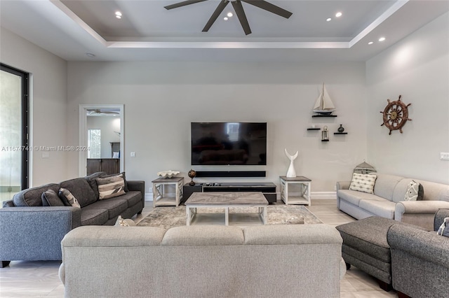 living room with a raised ceiling, plenty of natural light, and ceiling fan