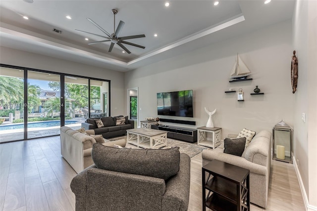 living room with ceiling fan, a tray ceiling, and light hardwood / wood-style floors