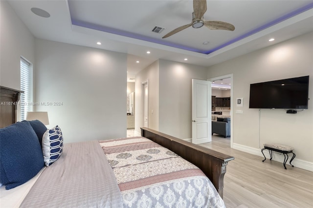 bedroom featuring light wood-type flooring, ceiling fan, and a tray ceiling