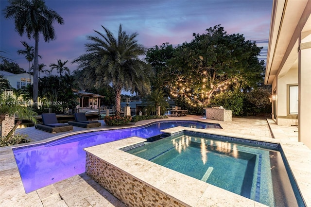 pool at dusk with an in ground hot tub and a patio