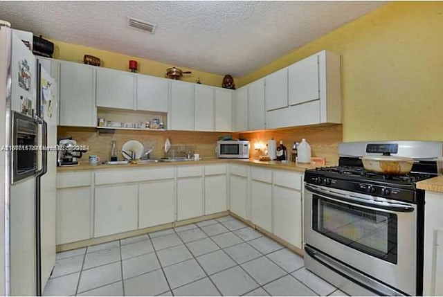 kitchen with a textured ceiling, white appliances, light tile patterned floors, and white cabinets