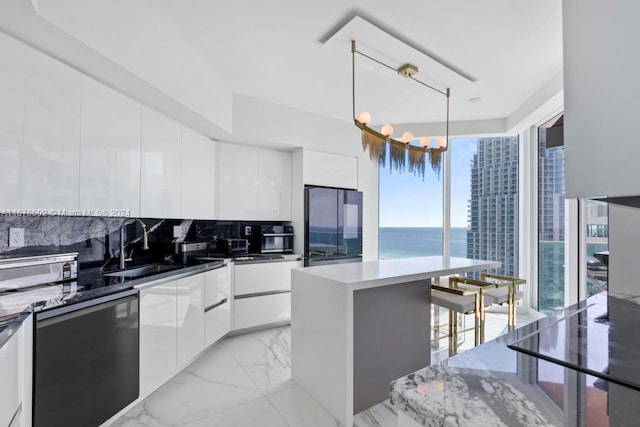 kitchen with decorative backsplash, a center island, decorative light fixtures, white cabinets, and a water view