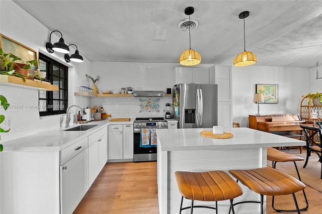 kitchen with white cabinets, hanging light fixtures, appliances with stainless steel finishes, light hardwood / wood-style floors, and sink