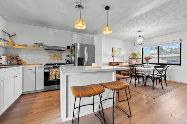 kitchen with ventilation hood, appliances with stainless steel finishes, pendant lighting, and white cabinetry