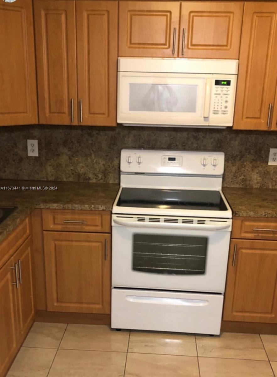 kitchen featuring dark stone countertops, light tile patterned flooring, backsplash, and white appliances