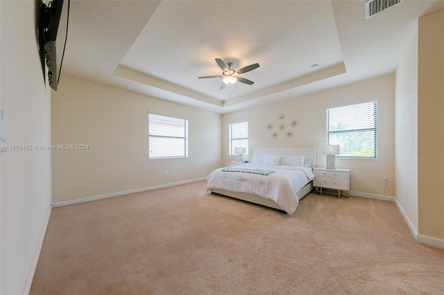 unfurnished bedroom featuring a tray ceiling, multiple windows, and ceiling fan