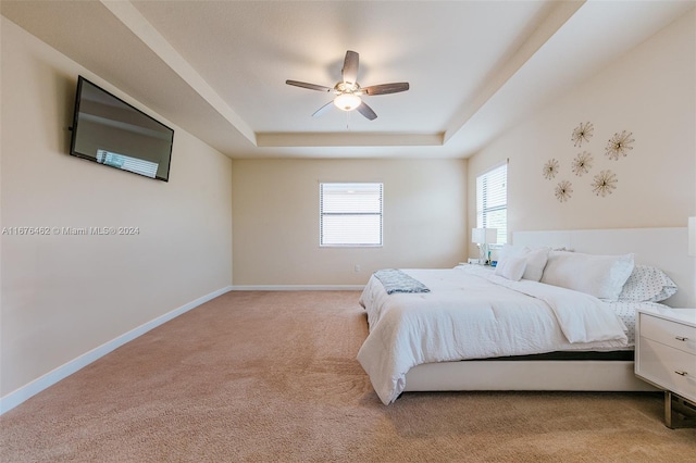 carpeted bedroom featuring ceiling fan and a raised ceiling