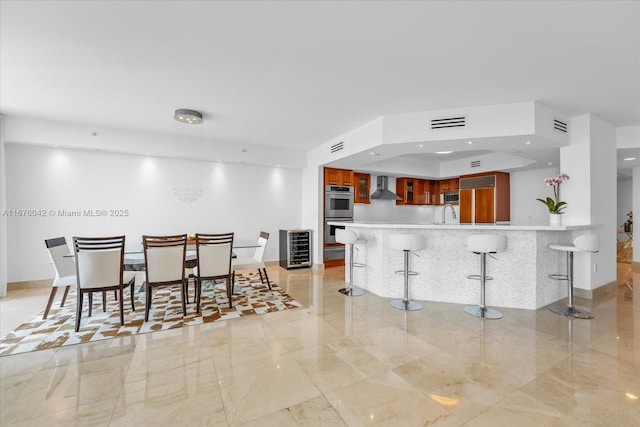 kitchen featuring sink, wall chimney range hood, kitchen peninsula, a breakfast bar area, and appliances with stainless steel finishes