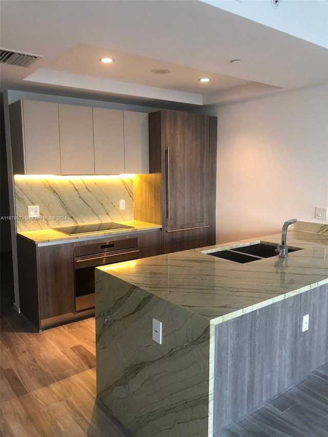 kitchen featuring light hardwood / wood-style flooring, a tray ceiling, stainless steel oven, decorative backsplash, and cooktop