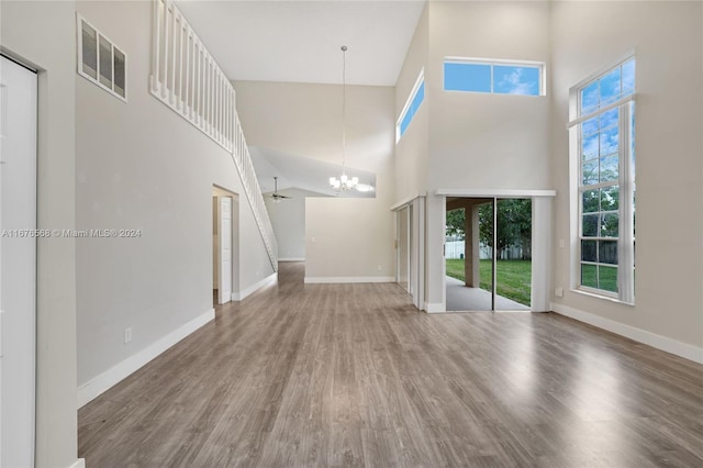 unfurnished living room featuring wood-type flooring, a high ceiling, and ceiling fan with notable chandelier