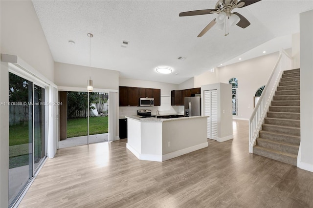 kitchen featuring light hardwood / wood-style floors, appliances with stainless steel finishes, pendant lighting, and a kitchen island with sink