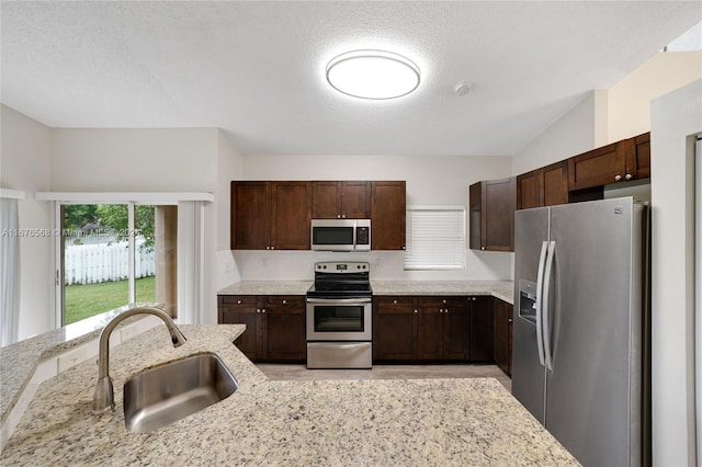 kitchen featuring sink, appliances with stainless steel finishes, light stone counters, and a textured ceiling