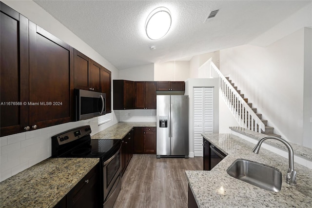 kitchen featuring lofted ceiling, hardwood / wood-style floors, appliances with stainless steel finishes, sink, and light stone counters