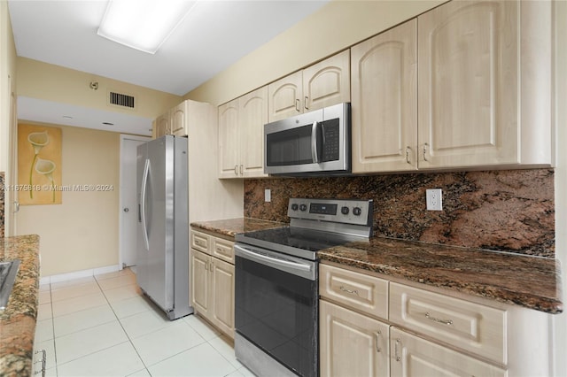 kitchen with tasteful backsplash, dark stone counters, appliances with stainless steel finishes, and light tile patterned floors