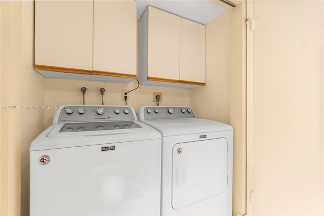 clothes washing area with washer and clothes dryer and cabinets