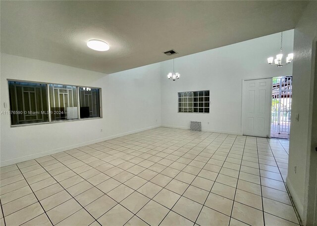 tiled empty room with a textured ceiling and an inviting chandelier