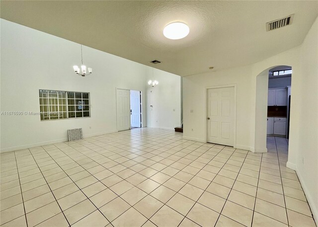 tiled empty room with a textured ceiling and an inviting chandelier