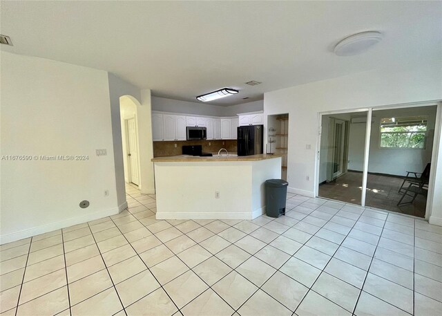 kitchen with kitchen peninsula, tasteful backsplash, black appliances, light tile patterned floors, and white cabinetry