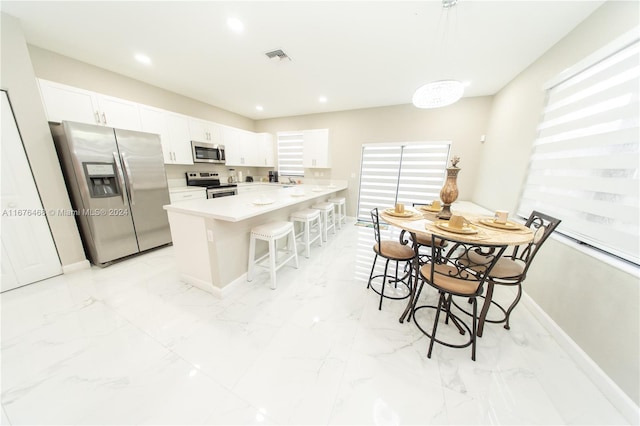 kitchen with decorative light fixtures, stainless steel appliances, kitchen peninsula, white cabinets, and a kitchen bar