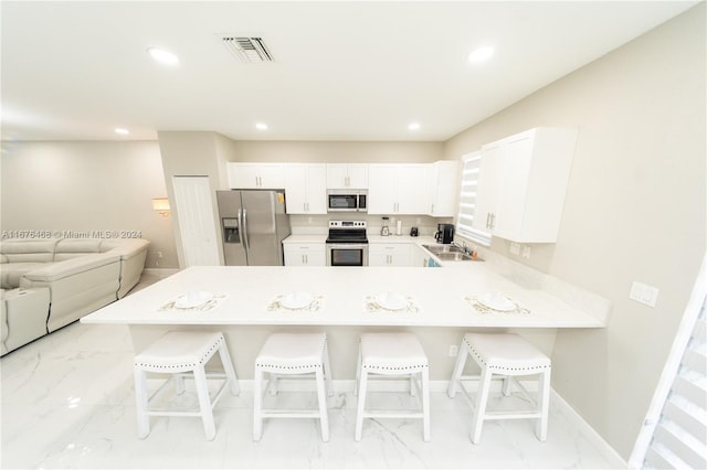 kitchen with appliances with stainless steel finishes, kitchen peninsula, white cabinetry, and a breakfast bar