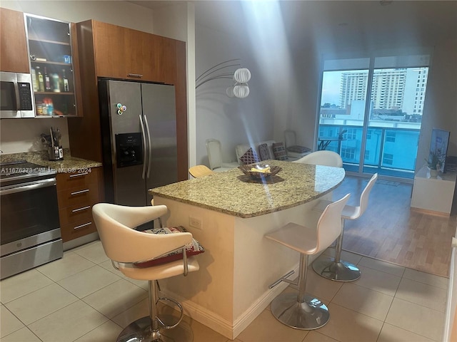 kitchen featuring a kitchen island, a kitchen bar, stainless steel appliances, light hardwood / wood-style floors, and light stone counters