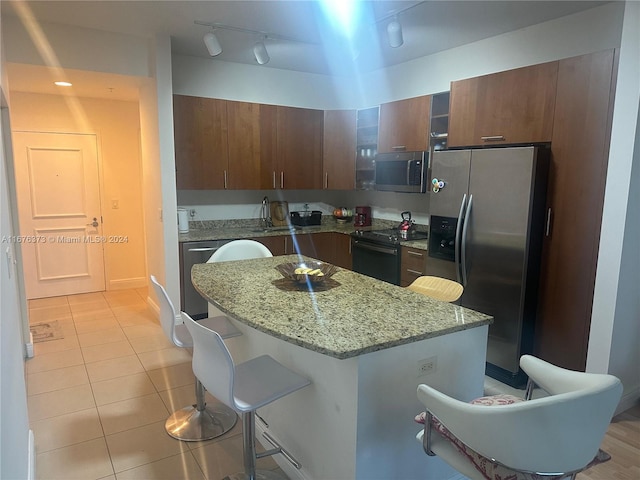 kitchen with a kitchen island, a breakfast bar area, light stone countertops, light tile patterned flooring, and appliances with stainless steel finishes