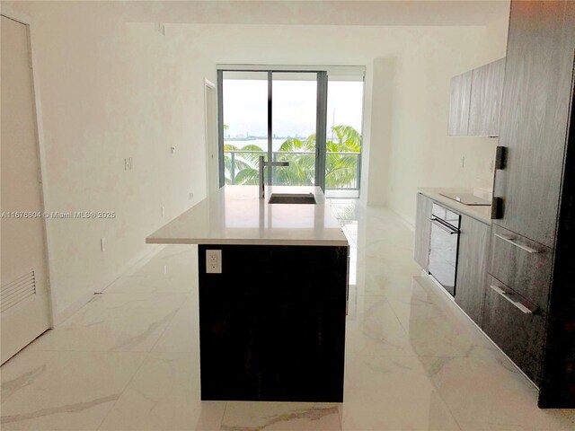 kitchen featuring stainless steel oven, black electric stovetop, sink, and a kitchen island with sink