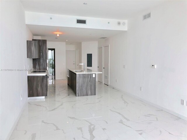 kitchen featuring dark brown cabinetry, sink, electric panel, and a kitchen island with sink