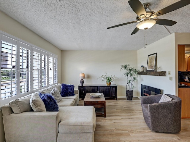 living room with light hardwood / wood-style floors, ceiling fan, and a textured ceiling