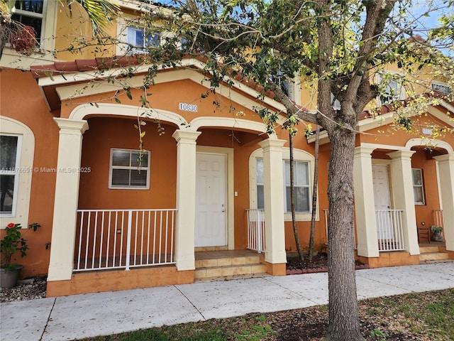 doorway to property with covered porch and stucco siding