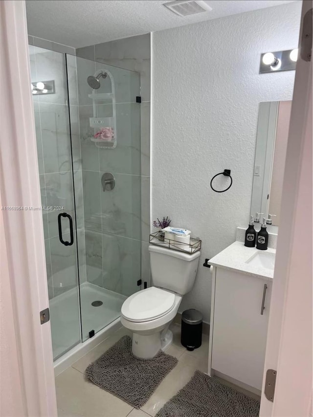 bathroom with a textured ceiling, toilet, vanity, an enclosed shower, and tile patterned flooring