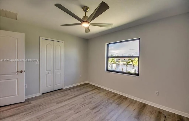 unfurnished bedroom with light hardwood / wood-style flooring, a water view, ceiling fan, and a closet