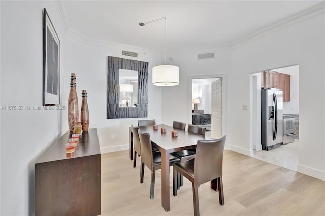 dining space featuring light wood-type flooring, ornamental molding, and visible vents