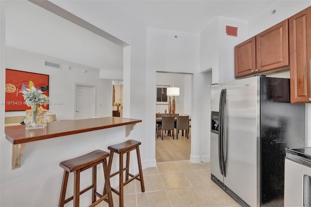 kitchen featuring kitchen peninsula, crown molding, light tile patterned flooring, a kitchen bar, and appliances with stainless steel finishes