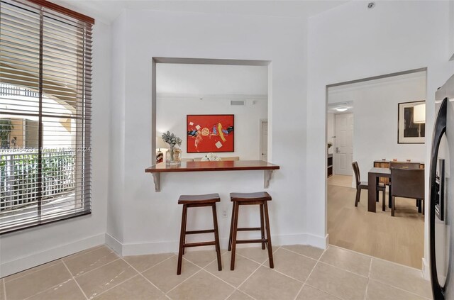 kitchen featuring kitchen peninsula, stainless steel fridge, a kitchen bar, and light tile patterned floors