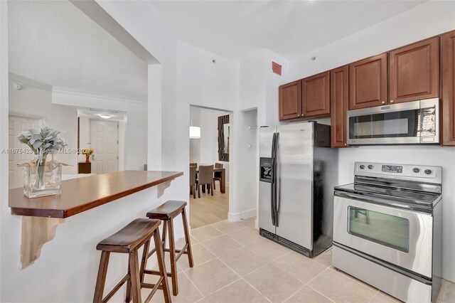 kitchen with appliances with stainless steel finishes, light tile patterned floors, a kitchen bar, and ornamental molding