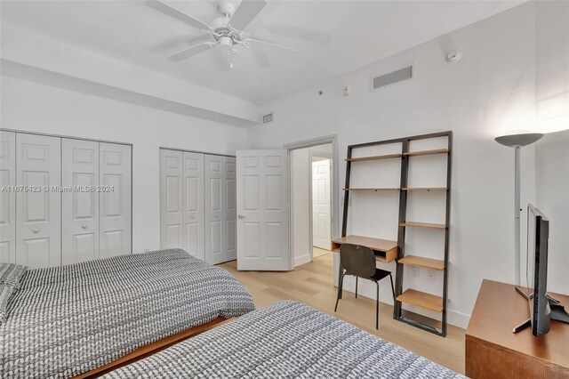 bedroom featuring two closets, light wood-type flooring, and ceiling fan