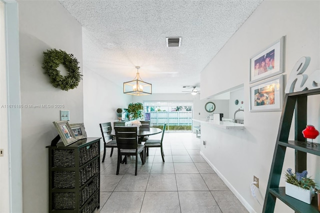 dining room with light tile patterned floors, baseboards, visible vents, a textured ceiling, and ceiling fan with notable chandelier