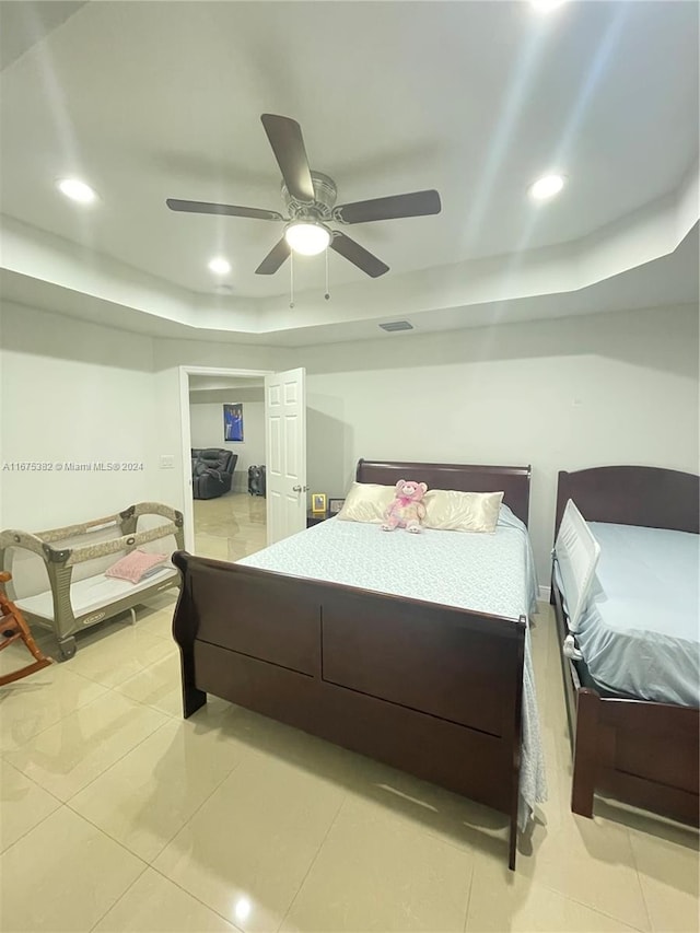 bedroom with ceiling fan, a tray ceiling, and light tile patterned floors