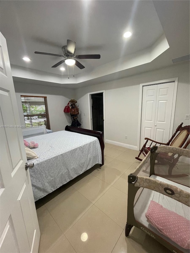 tiled bedroom with a closet, ceiling fan, and a raised ceiling