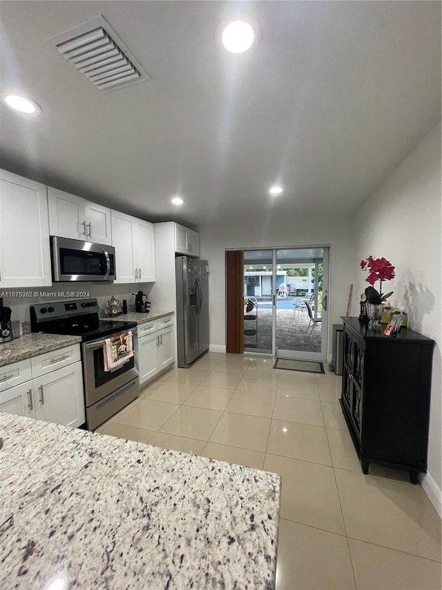 kitchen featuring light stone counters, stainless steel appliances, light tile patterned flooring, and white cabinets