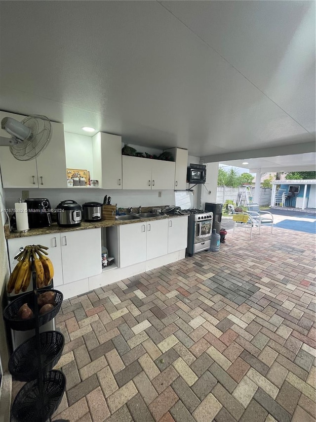 1369 Rainbow Ave, Palm Beach, FL 33406 - kitchen featuring stainless steel gas range oven, open shelves, dark countertops, and white cabinetry
