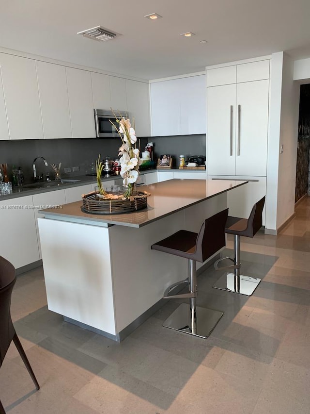 kitchen featuring white cabinets, a kitchen breakfast bar, a kitchen island, and sink