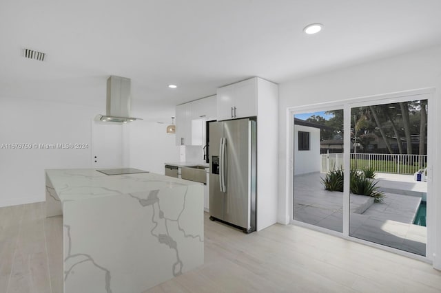 kitchen featuring appliances with stainless steel finishes, white cabinetry, light stone countertops, light wood-type flooring, and wall chimney exhaust hood