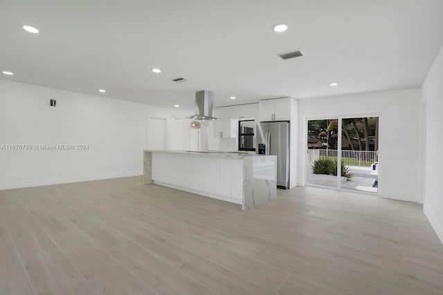 kitchen with wall chimney exhaust hood, stainless steel fridge, white cabinetry, and light hardwood / wood-style flooring