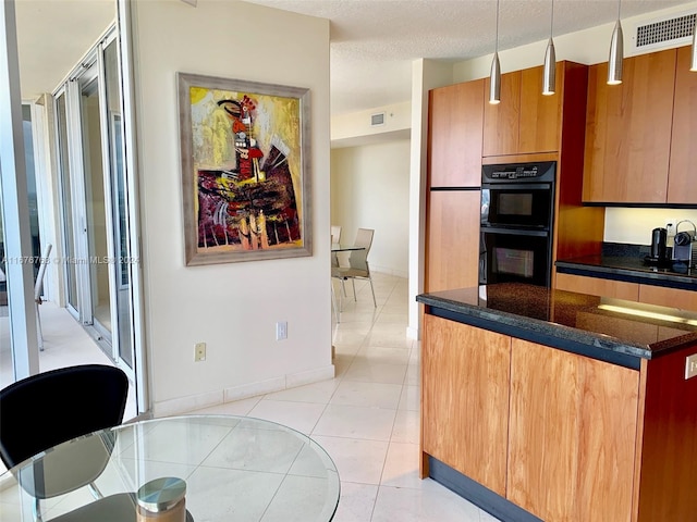 kitchen featuring hanging light fixtures, dark stone countertops, light tile patterned floors, black double oven, and a textured ceiling