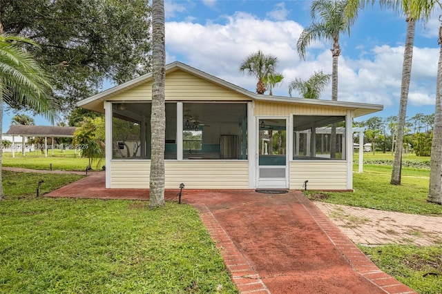 rear view of property featuring ceiling fan, a sunroom, and a lawn