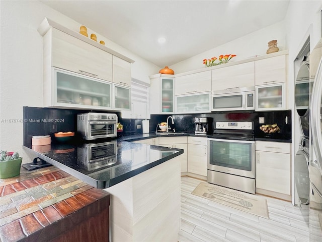 kitchen with lofted ceiling, sink, stainless steel electric range, stacked washer / dryer, and tasteful backsplash